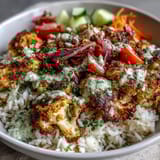 A colorful bowl of the Roasted Cauliflower Bowl, featuring aromatic cauliflower, crisp cucumbers, and cherry tomatoes beside a vibrant green spinach bed.