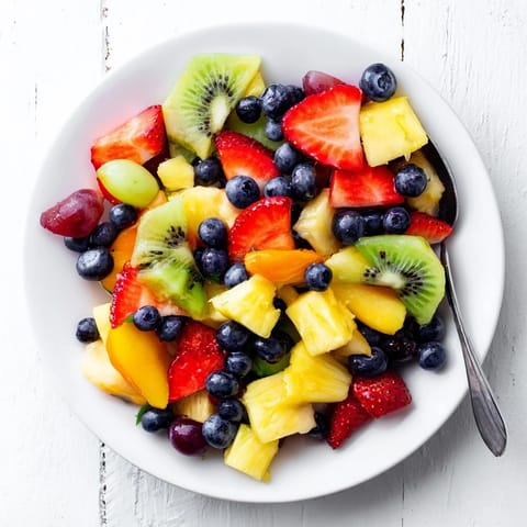 Vibrant Fruit Salad with strawberries, pineapple, and kiwi glistening with citrus syrup in a clear glass bowl.