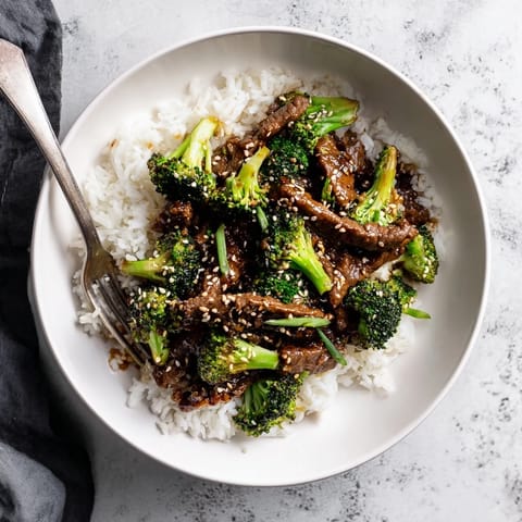 Golden-brown Beef and Broccoli stir-fry sizzling in a wok, garnished with sesame seeds and fresh green onions for extra flavor.