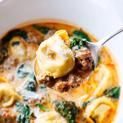 Spoonful of cheesy tortellini in a creamy tomato broth with wilted spinach.