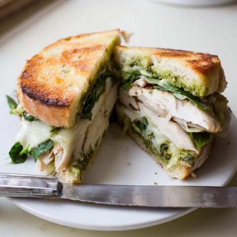 Sliced Chicken Pesto Panini reveals juicy chicken, gooey cheese, and optional spinach on warm bread.