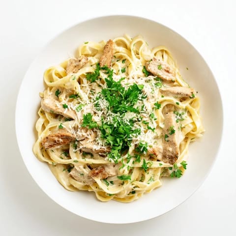 A fork lifts a bite of Cajun Chicken Alfredo, showcasing silky sauce clinging to pasta and seasoned chicken slices.