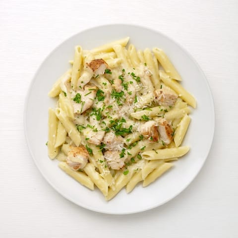 Golden roasted garlic chicken penne pasta tossed in a creamy, silky sauce, garnished with fresh parsley and extra Parmesan cheese.