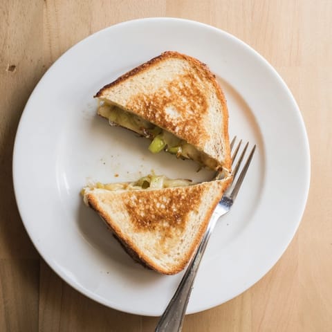 A close-up of a Havarti & Caramelized Leek Grilled Cheese sandwich, showcasing the golden crust and melted, gooey cheese filling.