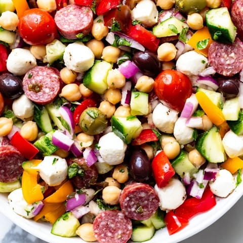 A serving bowl of Crunchy Antipasto Chopped Salad over a rustic wooden table highlights fresh basil and pepperoncini for a vibrant appetizer.