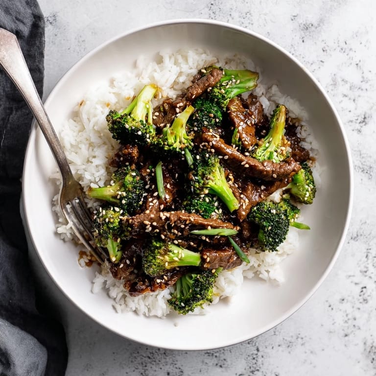 Golden-brown Beef and Broccoli stir-fry sizzling in a wok, garnished with sesame seeds and fresh green onions for extra flavor.