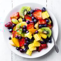 Vibrant Fruit Salad with strawberries, pineapple, and kiwi glistening with citrus syrup in a clear glass bowl.