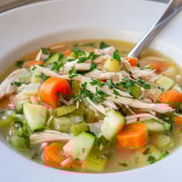 This Spring Garden Chicken Soup features tender shredded chicken, carrots, and bright green peas in a clear broth, garnished with fresh parsley.