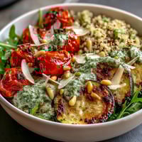 Freshly cooked quinoa, roasted zucchini, and red peppers topped with peppery arugula pesto in a grain bowl.